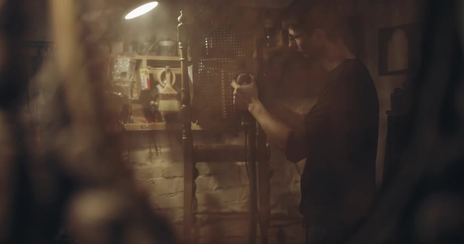 Man can be seen through back of one chair working on another with a power tool