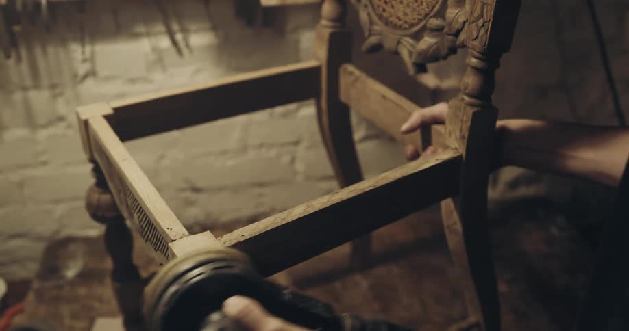 A man in a wood working shop polishes a chair that he is making