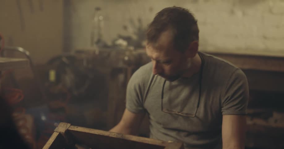 Man in t shirt works on wooden chair in workshop