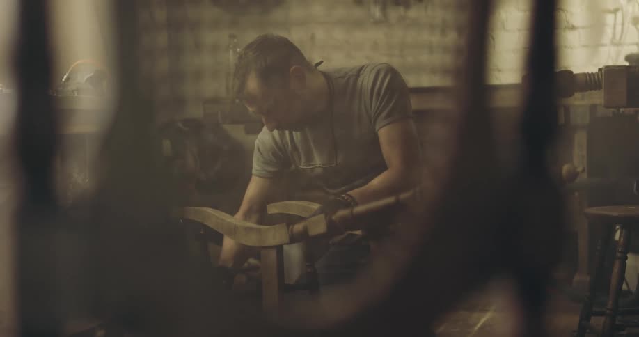 A man uses a rag to apply a stain to a wooden chair in his shop