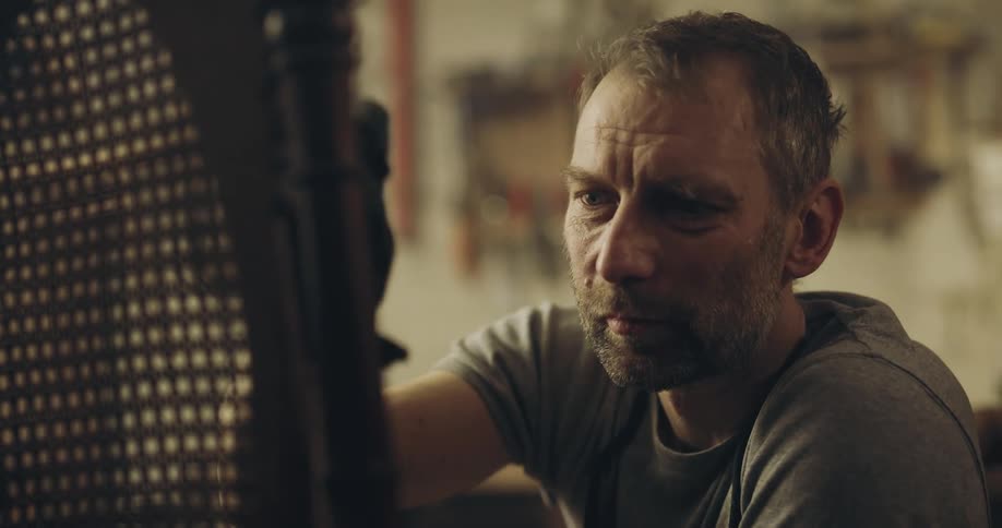 Man works on wicker backed chair in workshop
