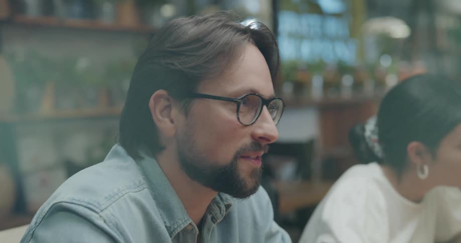 A man and a woman sitting indoors talking with others