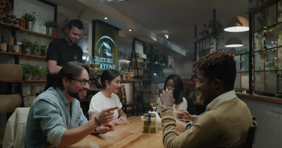 A waiter hands out glasses of wine to a table of friends in a restaurant