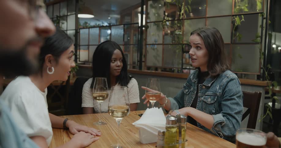 A group of people sit together talking at a restaurant table with wine glasses