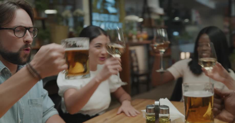 A group of people clink their glasses of liquor together as talk and laugh together in a restaurant