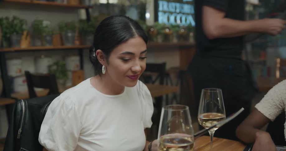 A group of young adults sit at a restaurant table with wine glasses and look over the menu