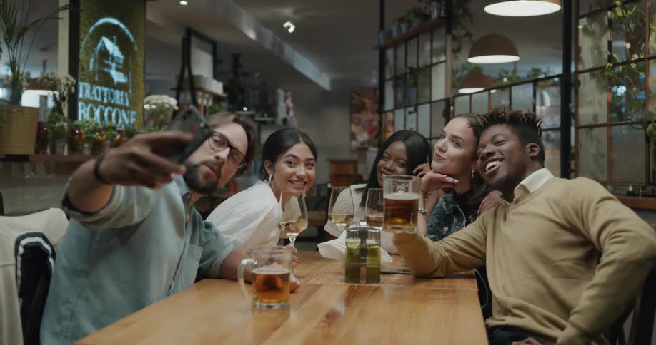 Two men and three women sitting at a table taking a picture with a smart phone