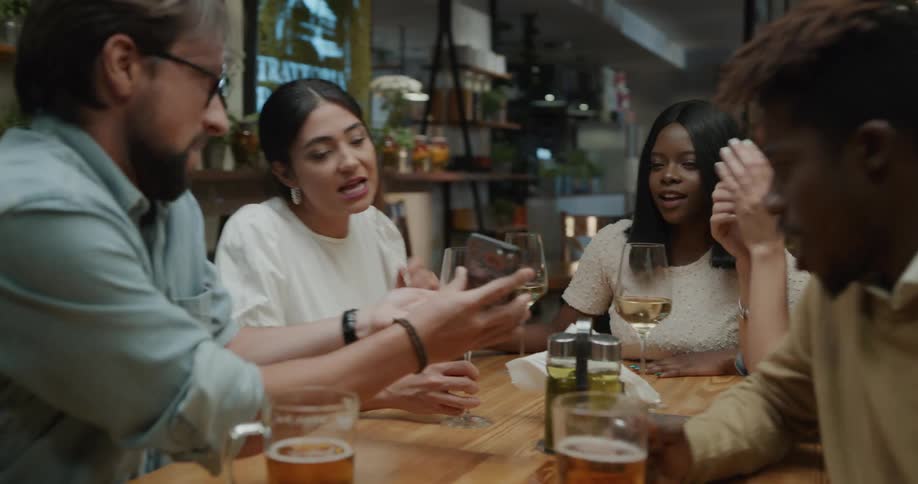 A man pulls out his cell phone and takes a selfie as him and his friends drink at a bar