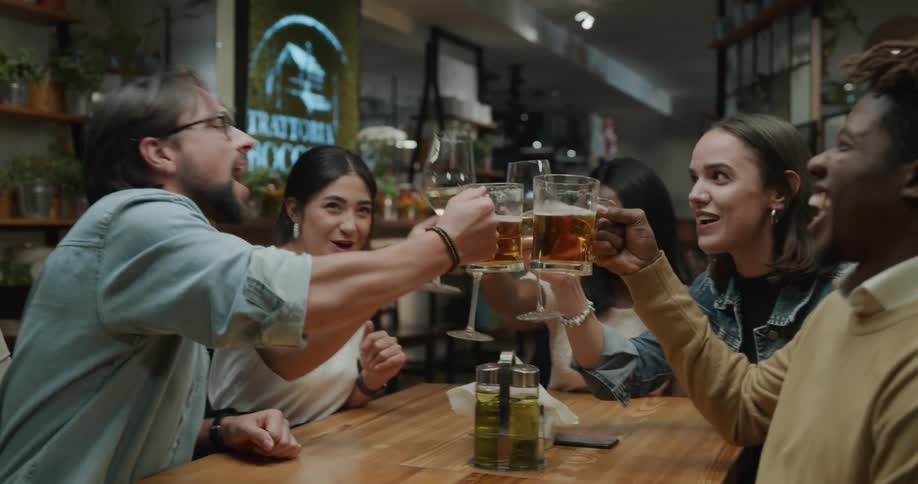 A group of men and women clink their glasses of liquor together as they chat and laugh together at a table in a restaurant