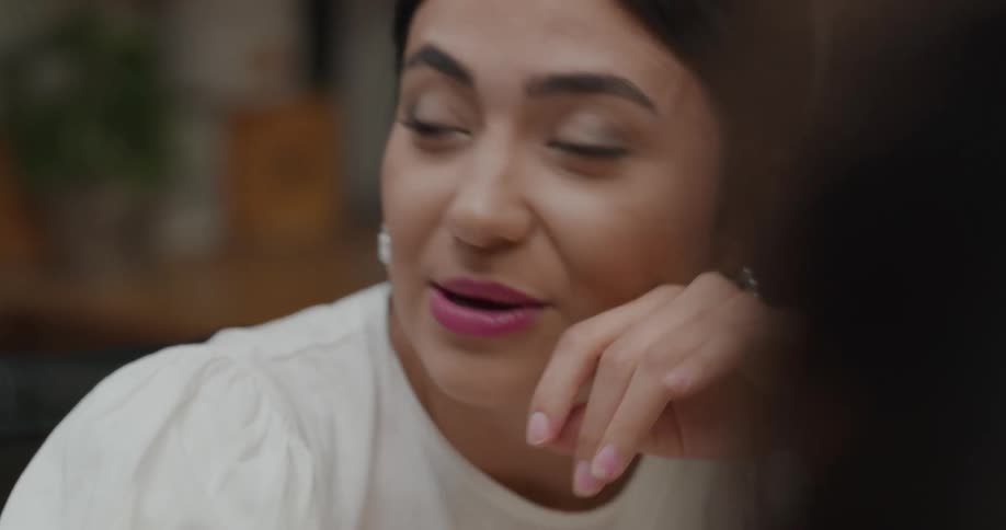 Woman wearing lipstick sits laughing and talking near wine glass