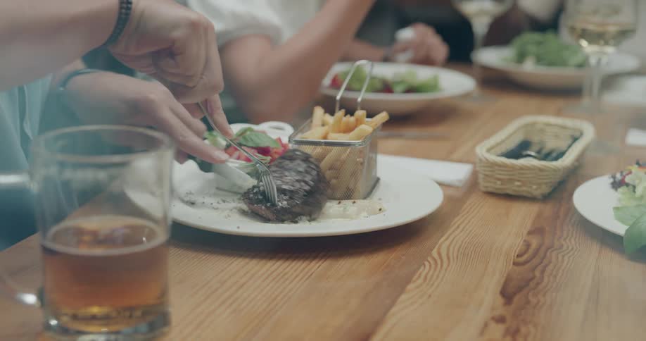 A man cuts into his steak while having dinner with friends at a restaurant