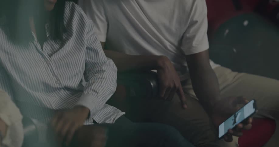 Couple sitting in darkened movie theater laughs over video on mobile phone