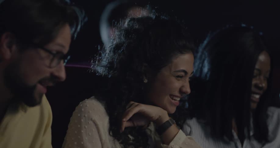 People in dark theater smile and laugh while looking at mobile phone