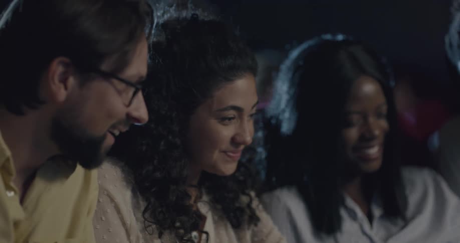 A group of men and women are sitting in a theater talking and laughing amongst each other