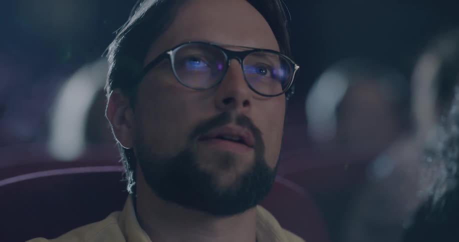 Man with a beard and glasses eats popcorn and watches a movie in the movie theater