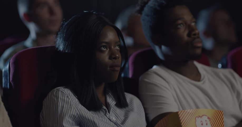 Man and woman holding popcorn bag watch a movie in the movie theater