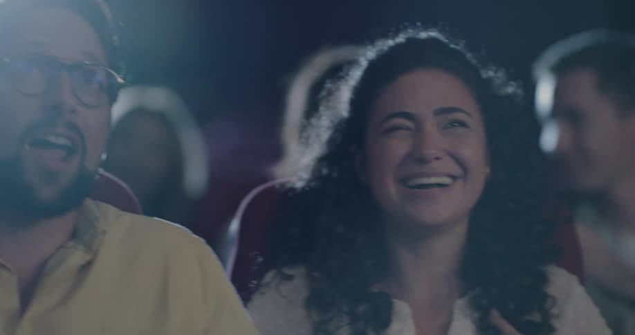 People sitting in dark movie theater laugh and talk to each other