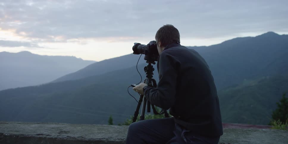 Man sitting on a wall while taking far-off photos of a landscape