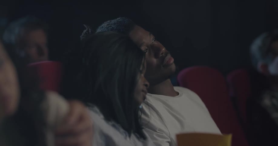 A man kisses a womans hand as they sit in a movie theater