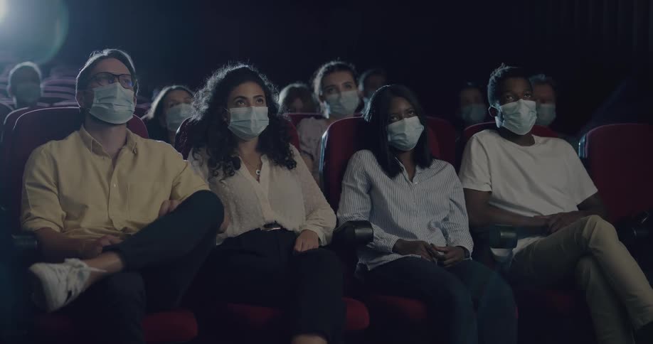 Audience wearing face masks sits in dark theater
