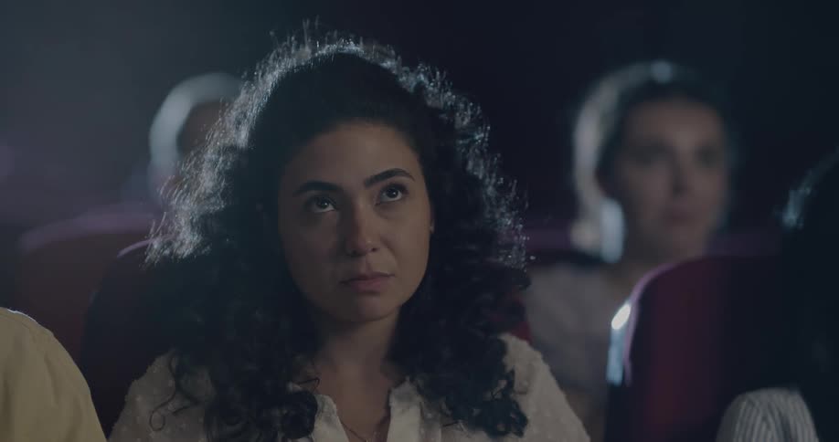 Woman with curly hair is scared while watching a movie in the movie theater