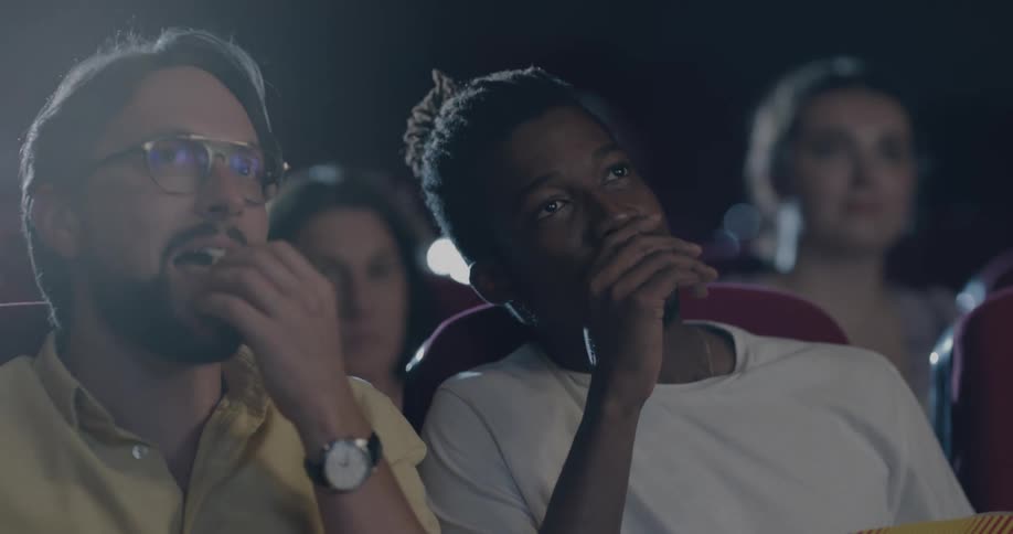 Two men talking and eating popcorn in a movie theater