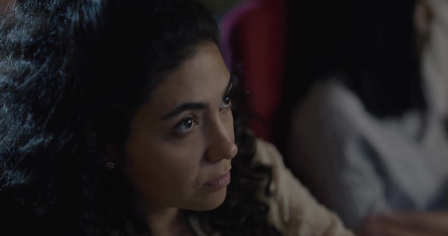 Woman sits in theater audience watching movie while eating popcorn