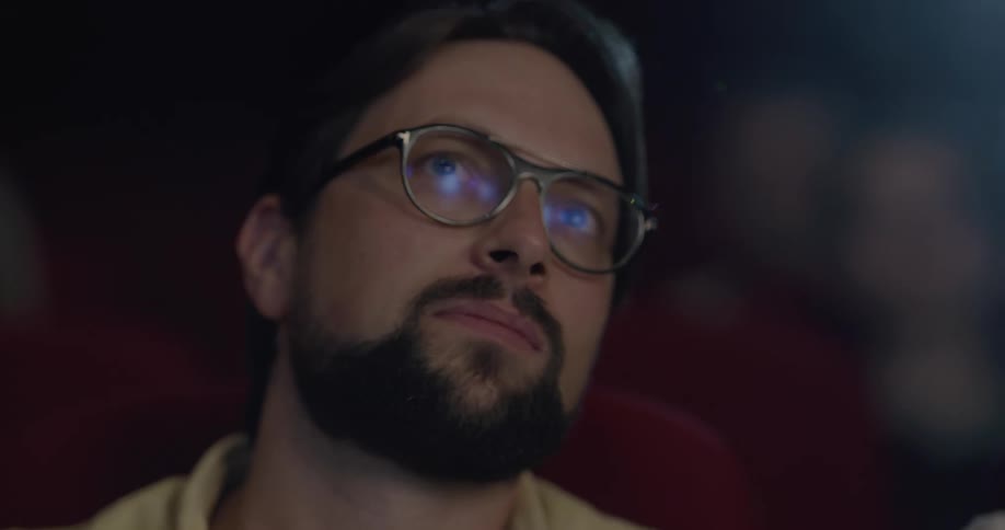 Two men talk and laugh and eat popcorn at a movie theater