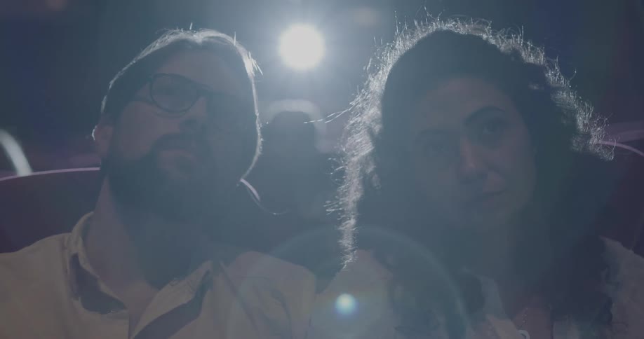 A man and woman watch a movie while sitting together in a cinema theater