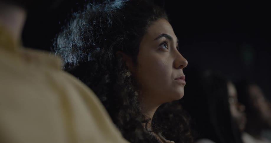 A young woman eats popcorn while watching a movie in a theater