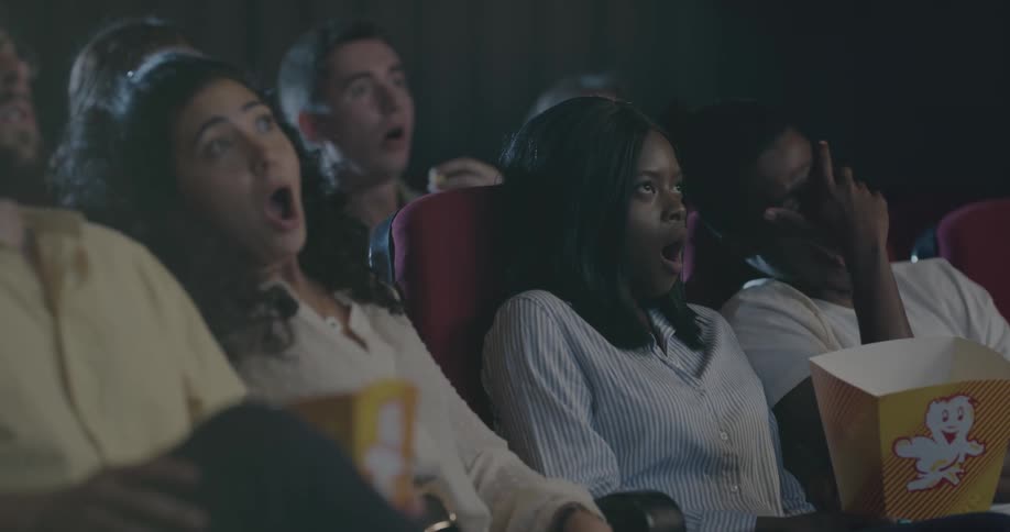 Audience watching movie in dark theater shocked by film