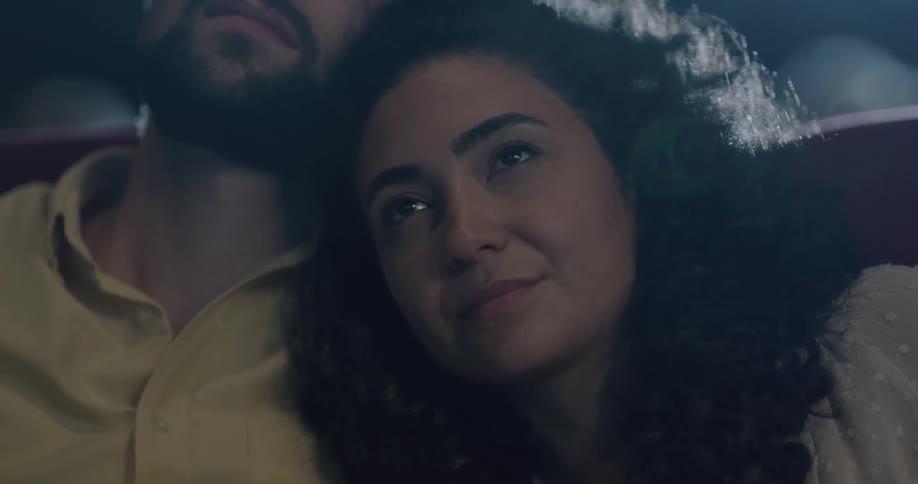A woman leans against her boyfriend in a movie theater