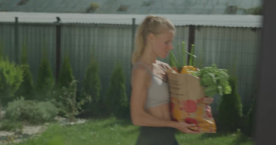 A woman carries a bag of groceries across the outside yard