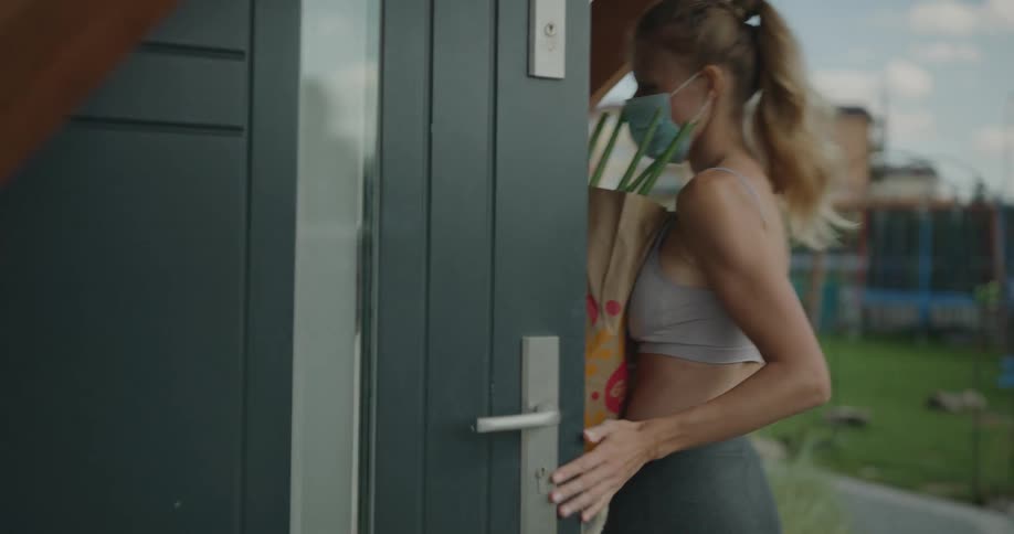A woman carries a bag of groceries in to her house