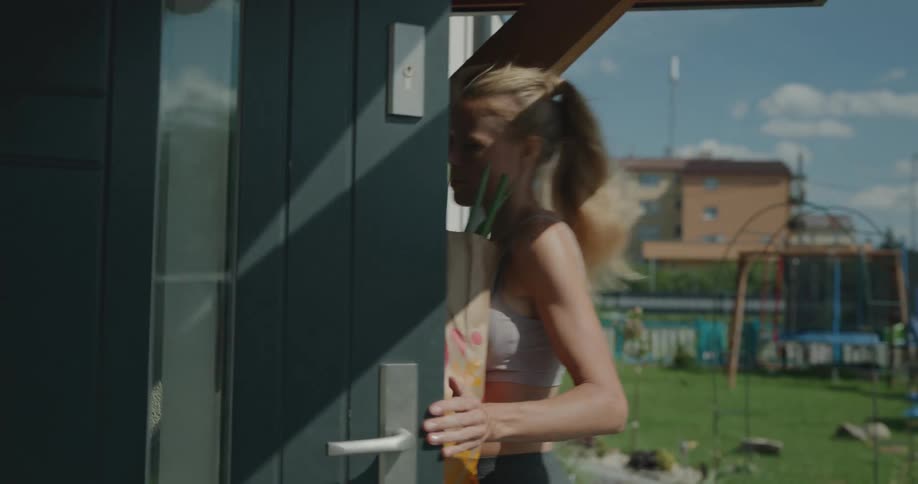 A young woman carries of a bag of groceries in to her house