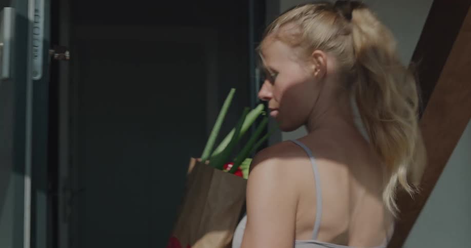 A woman carries a bag of groceries to her front door and walks inside