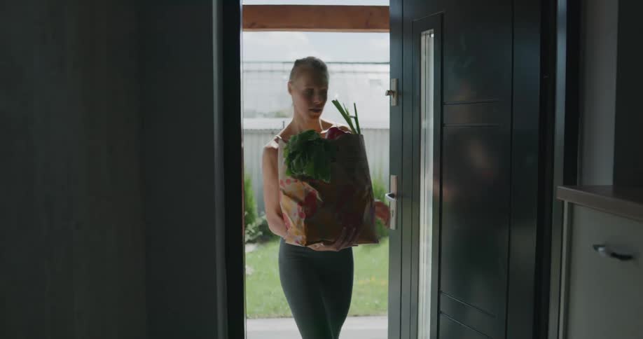 A woman walks in to her home carrying a bag of groceries