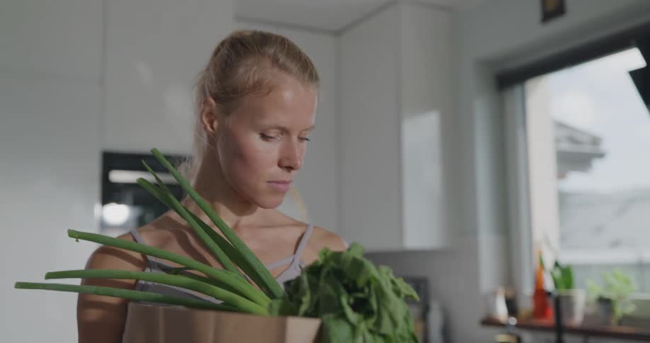 Blonde woman with a ponytail takes out vegetables from the bag in the kitchen