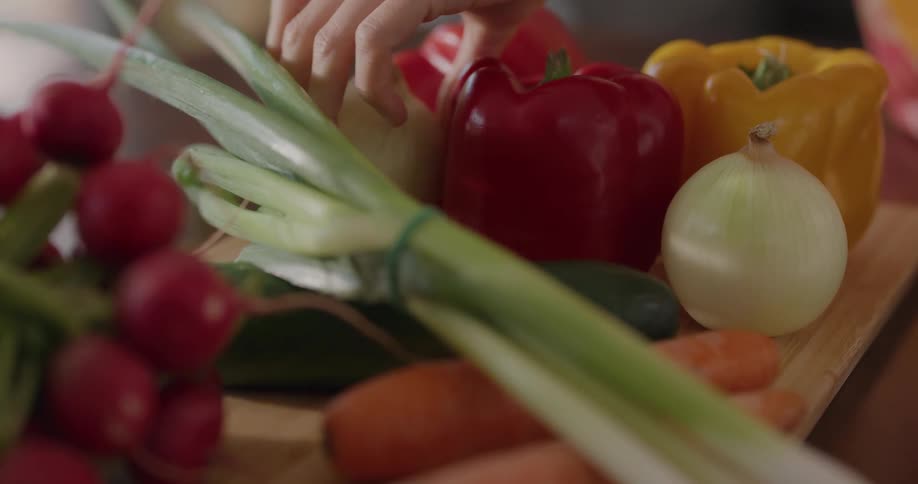 Woman places fresh vegetables over a cutting board on the kitchen at home