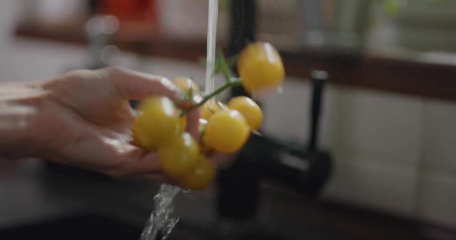 A woman washing yellow cherry tomatoes in a kitchen sink at home