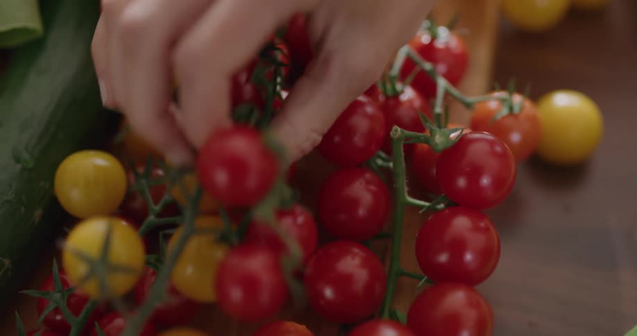 A hand picks up different colored tomatoes on a vine from a flat surface