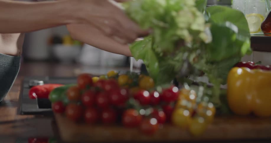 A woman in yoga pants and a sports bra washing vegetables at a kitchen sink