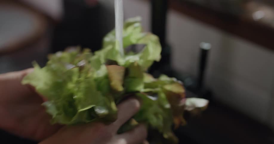 Woman washes a yellow bell pepper and a lettuce in the kitchen