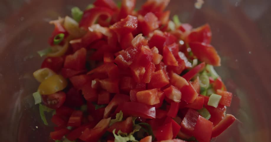 Woman puts chopped red bell pepper on the salad in the bowl