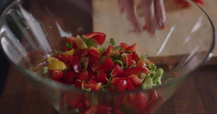 Woman cuts a red bell pepper and puts it on the salad in the bowl