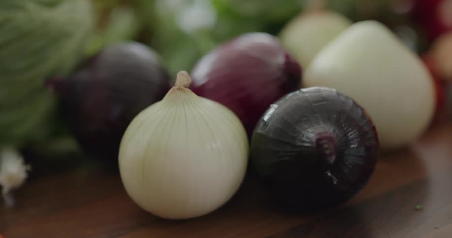 A person retrieves a red onion from a group of onion lying on a wooden table