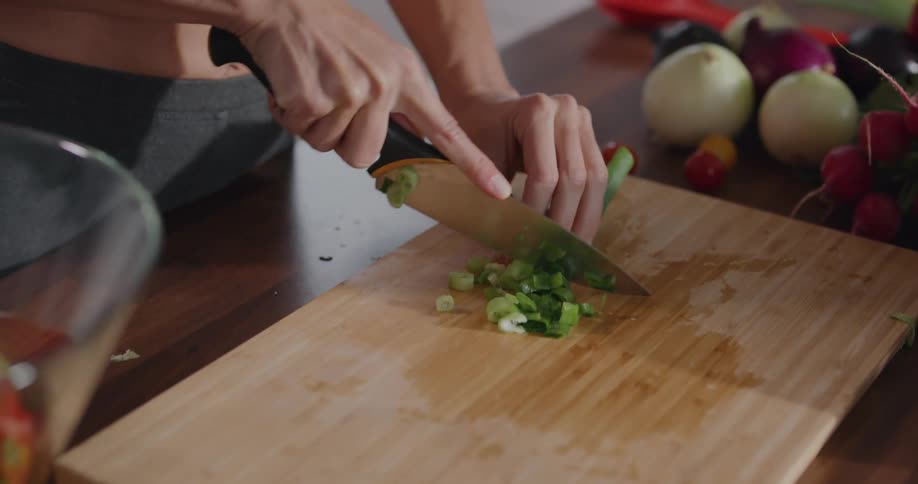 A woman at home chops onions and puts them in a salad