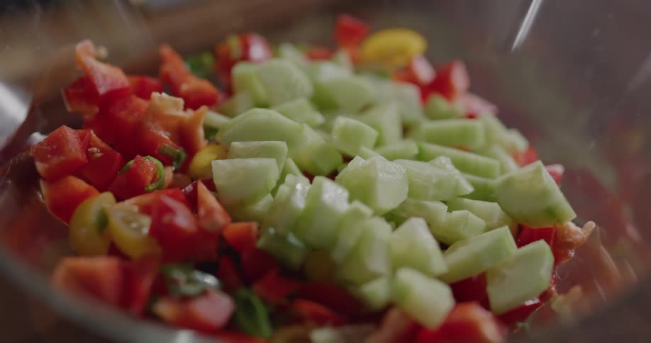 A woman at home putting cucumbers in to a bowl with vegetables in it