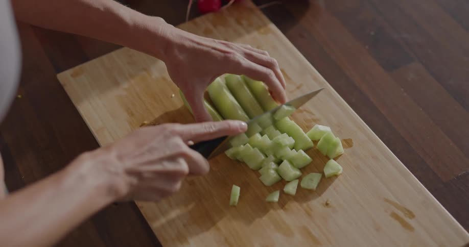 Person slices produce on chopping board set on wooden counter