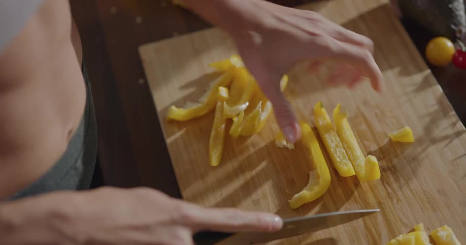 Woman cuts yellow bell pepper on a cutting board in the kitchen